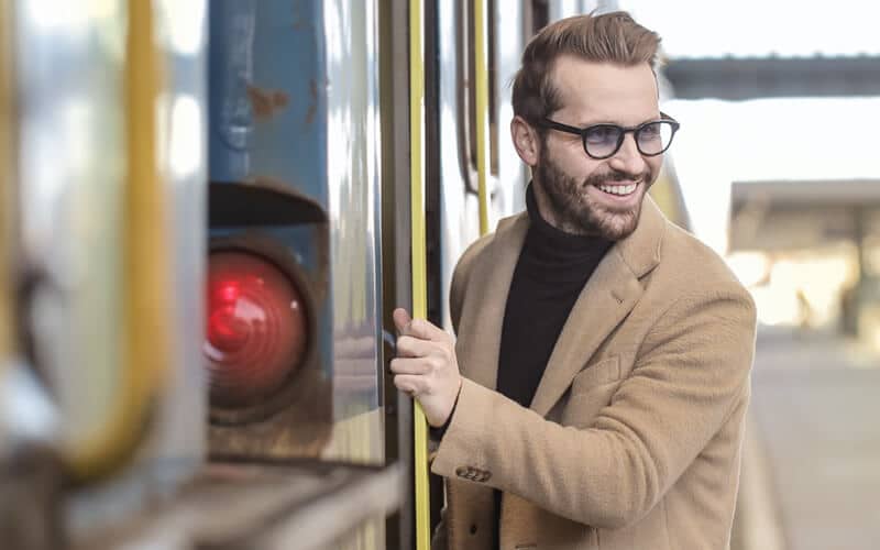 Bruinharige man met een bruine blazer en bril glimlachend naast de trein